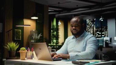 Siyahi işadamı saati kontrol ediyor ve ofisteki masa lambasını kapatıyor, yeni bir bakış açısı için strateji kuruyor ve işlerini bitiriyor. Mesai saatleri dışında mesai yapan biri. Kamera A.