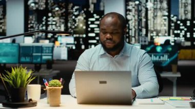 Siyahi iş danışmanı mesai saatleri dışında çalışıyor. İnternet bilgilerini kontrol ediyor, önemli verileri dizüstü bilgisayara yazıyor. Girişimci hedeflerle aynı hizaya getirmek için bir özet oluşturup strateji tasarlamak. Kamera B.