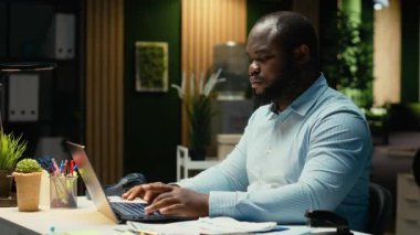 Erkek Afrikalı Amerikalı işçi e-postaları okuyor ve yöneticilik görevlerini yürütüyor. Çok uluslu bir şirketin görüşlerini belgeliyor. Akşamları iş amaçlarını araştırıyorum. Kamera B.