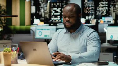 Siyahi ofis çalışanı, mesai saatleri dışında akıllı telefonları kontrol ederek, gece yarısı fazla mesai yaparken sosyal hizmetlerle bağlantılı bir bildirimi kontrol ediyor. Genç adam mesajları okuyor. Kamera B.