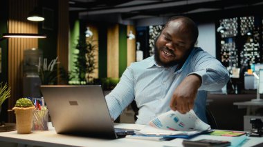 Erkek çalışan, gece geç saatlerde uzaktan sohbet için telefonla ortağını arıyor. Telefon hattındaki işbirliği sırasında gülümsüyor ve görüşünü paylaşıyor. Adaptasyon ve özen.