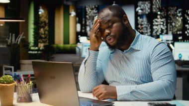 Siyahi sorunlu işçi, yoğun iş yükü veya başarısızlık nedeniyle yorgunluk ve rahatsızlığını ifade ederek, hayal kırıklığı ve yorgunluk içinde başını ovuşturuyor. Öfkeli adam baskı altında hisseder..