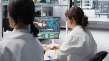 Tıbbi laboratuvar teknisyeni vardiyayı bitirmeyi bekliyor, hasta verilerini işliyor. Genetik analiz için PC kullanan araştırma tesisi çalışanı kol saati kontrolü, kamera B