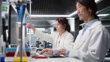 Kimya mühendisi araştırma tesisinde mavi işaret çözeltisi olan cam laboratuvar kullanıyor. Laboratuvarda kimyasal sıvı içeren silindiri inceleyen kimyager madde özelliklerini analiz ediyor, kamera A