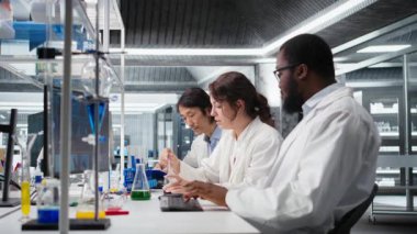 Kıdemli araştırmacı, iş arkadaşları tarafından yapılan laboratuvar deneylerinin gözlemlerini kaydeder. Laboratuvardaki Asyalı adam veri kaydı yapıyor. Meslektaşları tarafından yapılan kimyasal testleri not alıyor. Kamera A.