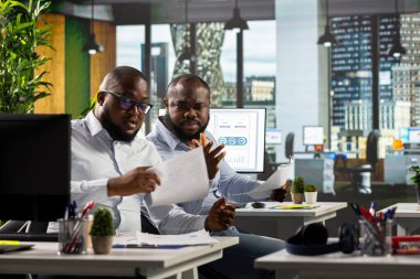 Şirket ofisindeki veri diyagramlarını kullanarak iş istihbaratı ve analiziyle uğraşan iki siyah çalışan genel şirket stratejisini geliştirmek için projeleri ve raporları gözden geçirir..