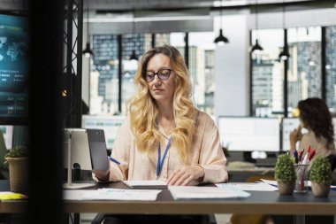 Kadın işletme müdürü tabletine veri analizine dalmış, stratejik planlama için çalışma yerinde tek başına oturuyor. Hedefe yönelik zihniyet çok uluslu şirkete başarı sağlar.