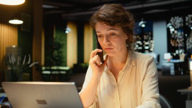 İş kadını, iş ortağıyla uzaktan görüşme için telefona cevap veriyor. Telefon hattında iş birliği yaparken gülümsüyor. Profesyonel bağlantıya uyum ve özen. Kamera A.