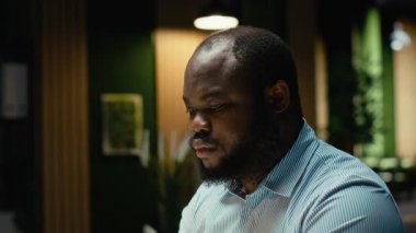 Afrikalı Amerikalı bir adam laptopta bilgi yazıyor ve raporları kontrol ediyor, yeni bir iş hedefi ya da hedefi için verileri gözden geçiriyor ve gözden geçiriyor. Mesai sonrası şirket yönetimi. Kamera B.