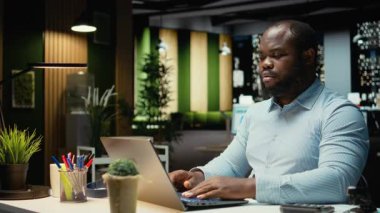 Siyahi bir danışman, gece geç saatlere kadar ayakta kalıp kurumsal işlerle ilgilenmek için bir fincan kahvenin tadını çıkarıyor. Geceleri kafein içeceğiyle düzeltme ve yazma. Kamera A.