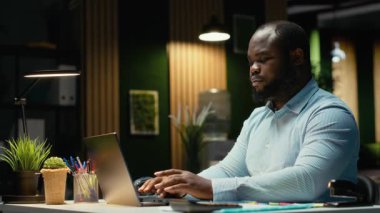 Afrika kökenli Amerikalı iş adamı işlerini bitiriyor ve masa lambasını kapatıyor. Kompleks proje için fazla mesai yaptıktan sonra gece geç saatlerde ofisten çıkıyor. İşi bitirdikten sonraki zamanı kontrol ediyorum. Kamera B.