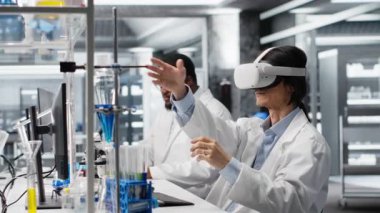 Laboratuvar uzmanı deney için kimyasal sıvılar kullanan VR kulaklık takıyor. Kimyager, iş yerindeki cam imalathanesi B kamerasını kullanarak sanal gerçeklik aygıtı kullanıyor.