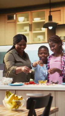 Dikey Video Ailesi, lezzetli ev yapımı pizzalar yaptıktan sonra el çırpıyor, sıcak bir mutfakta tezahürat yapıyor ve alkışlıyor. Siyahi ebeveynler ve çocuklar kahkaha ve sıcaklığı paylaşıyorlar. Kamera A.