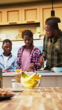 Dikey Video Afro-Amerikan ailesi pizza günü için online yemek tarifini takip ediyor, eğlenceli hafta sonu aktivitelerinin tadını çıkarıyor, mutfakta birlikte pizza yapıyorlar. Bağ kurmak için mutluluk ve takım çalışması