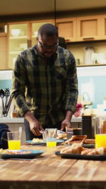 Dikey Video Babası, küçük oğlu için okul yemeği hazırlıyor ve sırt çantasını hazırlıyor. Aile fertleri, sıcak bir sabah kahvaltısının tadını çıkarıyorlar. Yemek hazırlık okulu çantası. Kamera A.