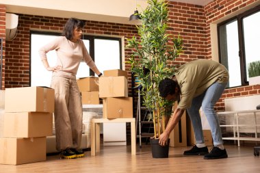 Kafkas kız arkadaşı etrafı karton kutularla çevrili bir şekilde izlerken siyah bir adam yere saksı yerleştiriyor. Yeni tuğla duvar dairesinde mobilya düzeni planlayan çok ırklı bir çift.