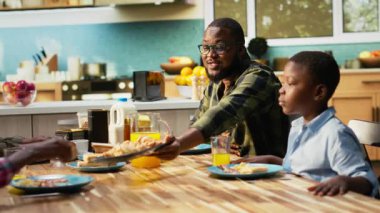 Aile güneşli bir mutfakta hafta sonu kahvaltısının tadını çıkarıyor. Çocuklar gülerken aileler kahve, kruvasan ve portakal suyu servis ediyor. Masanın etrafında aşk ve mutluluk anı. Kamera B.