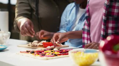 Siyah aile mutfakta birlikte ev yapımı pizza hazırlıyor, taze malzemeler ekliyor ve eğlenceli hafta sonu aktivitelerinde kahkahaların tadını çıkarıyor. Takım çalışması, neşe, aile zamanı ve mutluluk. Kamera B.