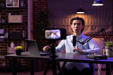 Modern Asyalı podcaster mikrofon ve dizüstü bilgisayarla birlikte dijital ses programları yaratıyor. Erkek vlogger çevrimiçi markalaşma, sosyal medya stratejisi ve yaratıcı işletmelere yönelik içerik sundu.