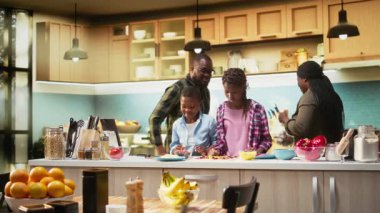 Siyah aile mutfakta pizza gününün tadını çıkarıyor ve ev yapımı pizza hazırlıyor. Ebeveynler ve çocuklar lezzetli bir yemek yaratırken aynı kahkahayı ve kaliteli bir bağ kurma zamanını paylaşıyorlar. Kamera A.