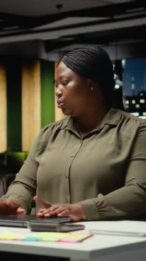 Dikey Video Siyah işletme yöneticisi gece geç saatlerde bilgisayarını kapatıp ofis lambasını kapatıyor ve binayı terk ediyor. Yorgun kadın gündemi tamamlamak için yönetim görevlerini tamamlıyor