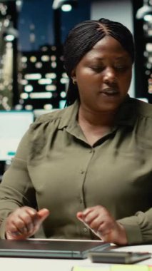 Dikey Video Siyah iş kadını ofis iş yerindeki bilgisayarını kapatıyor, gece yarısından sonra işini bitirip evine gidiyor. Fazla mesai yaptıktan sonra iş istasyonunu terk etmek. Kamera B.