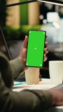 Afro-Amerikan bir kadının telefonundaki dikey video krom anahtar. Raporları kontrol ediyor, dizüstü bilgisayardaki performans ölçüleriyle çalışıyor. Bilgi toplanması ve idari görevlerin çözümü
