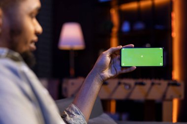 Siyah erkek serbest çalışan, evdeki uzay ekranını kopyalamak için akıllı telefon kullanıyor, rahat oturma odasında dinleniyor. Elinde cep telefonu ve telgraf tutan rahat bir çocuk..