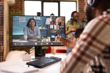 Serbest çalışan siyahi bir adam sanal Webinar sırasında oturma odasında oturuyor, kulaklık takıyor ve anlamlı jestler yapıyor. Erkek girişimci, uzak iş arkadaşlarına iş fikirlerini sunuyor..