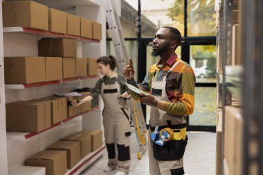 Lojistik tesisinde küçük teslimat hazırlıklarını yürüten siyahi bir çalışan, e-ticaret sevkiyatları, ürün perakende işleme ve çevrimiçi alışveriş müşterileri için ekspres teslimat üzerinde yoğunlaşıyor.