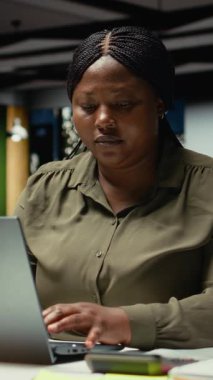 Dikey Video Siyah kadın analisti hedeflere ulaşmak için veri raporlarını düzeltiyor, mesai saatleri dışında bütçe hesaplama görevlerini çözüyor ve karanlık ofiste belgeleri kontrol ediyor. Strateji odası yönetimi