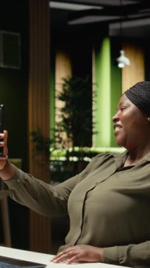 Dikey Video Girişimcisi telefonda konuşurken gülümsüyor video görüşmesi, dikkatlilik ve profesyonellik. Siyah kadın sanal sohbete daldı, katılımcılarla fikir alışverişinde bulundu.