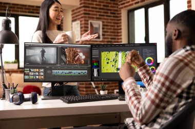 Kocasının çalışma yerinin arkasında durup iş arasında sohbet eden neşeli Asyalı kadın. Afrika kökenli Amerikalı erkek arkadaşı video montajından dinlenirken çok ırklı bir çift konuşuyor ve kahve içiyor..