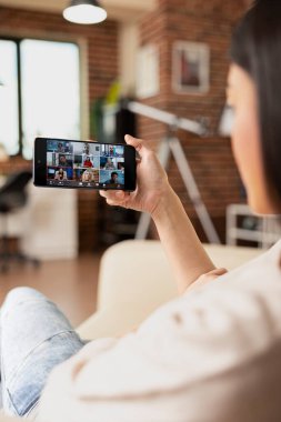 Uzaktan kumandalı kadın cep telefonuyla grup video görüşmesine katılıyor. Ofis brifinginde çok ırklı bir ekiple işbirliği yapıyor. Sanal hissedarlar toplantısına katılan serbest çalışan kadın.