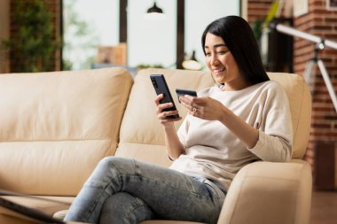 Uzaktaki Asyalı yönetici cep telefonu ve banka kartını kullanarak mutlu bir şekilde hareket ediyor. İç işlerindeki koltukta oturan kendine güvenen iş kadını, mali görevleri tamamlamak için internet araçlarına erişiyor..