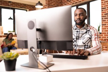 Evden uzaktan çalışan, tuğla duvarlı oturma odasındaki bilgisayar klavyesinde yazan siyahi bir girişimci. Serbest çalışan adam sunum hazırlıyor ve evden pazarlama planlarını araştırıyor..