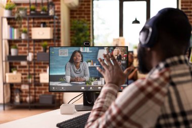 Profesyonel Afro-Amerikan adam masada oturuyor, video görüşmesi sırasında etkin bir şekilde konuşuyor. Sanal toplantıda uzak takım lideri, pazarlama ve iş stratejisinde hissedarlarla işbirliği yapıyor..