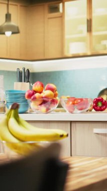 Dikey Video Parlak modern mutfak. Zarif mobilyalar ve ahşap dolaplar. Bir kesme tahtasında yemek takımı ve taze sebzeler, şık bir ev ve lüks bir ev tasarımı sergileniyor..