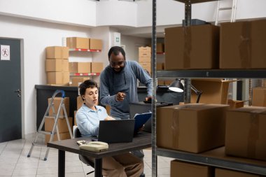 Yerel nakliye ve envanter işlemlerini yöneten bir depo dolusu kayıtlı kutu ve depolama birimleriyle dolu bir depoda çalışan çok ırklı işçiler..