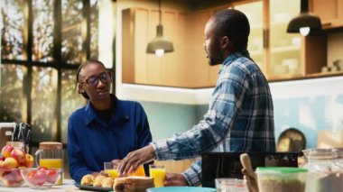 Erkek arkadaşı ve kız arkadaşı kahvaltı masası için ekmek hazırlıyor tost, ev yapımı hamur işi ve sabah kahvesinin tadını çıkarıyor. Sıcak bir mutfakta sevgi ve eğlence gösteren bir çift. Kamera B.