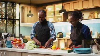 Siyah çift taze salata için bir kaseye doğranmış sebze ekliyor, kesme tahtasında birden fazla organik sebze var. Erkek arkadaş ve kız arkadaş vejetaryen yemeği yapıyor, yaşam tarzı. Kamera A.