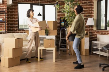 Kafkas kadın kahverengi kutuyu tutarken Afrikalı Amerikalı erkek arkadaşının saksı bitkisini yeni tuğla duvara taşımasını izliyor. Çok ırklı bir çift, eşyalarıyla birlikte taşınıyor..