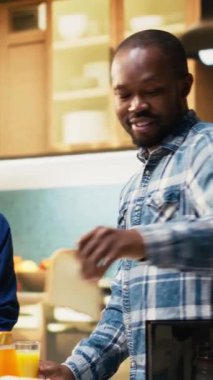 Dikey Gülümseyen Siyah Çift evde ev yapımı hamur işi ve tost ile sağlıklı bir kahvaltı hazırlıyor. Kahkaha, aşk ve rahat yaşam tarzı gösterisi sakin bir hafta sonu sabahı