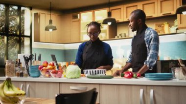 Neşeli siyah çift bir salata kasesi için avokado ve diğer sebzeleri kesiyor, vejetaryen yemeği için renkli ürünlerle pişiriyor. Sağlıklı organik yiyecekler için kahkaha ve sevgi. Kamera A.