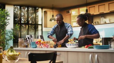 Mutlu siyah adam taze sebzelerin üzerine limon suyu sıkıyor, kız arkadaşıyla lezzetli bir salata hazırlıyor. Biyolojik organik içerikli baharatlı öğle yemeği, dinlenme anı. Kamera A.