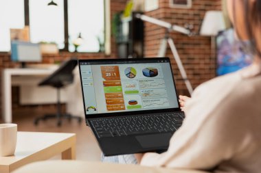 Genç bayan girişimci tuğladan duvar dairesindeki kanepede oturuyor, uzaktan bilgisayarla çalışıyor. Serbest çalışan kadın mali tabloları gözden geçiriyor ve iş stratejisini internette güncelliyor.