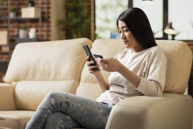 Koltukta oturan, cep telefonuyla yazan, online bankacılık için kart bilgilerini ekleyen odaklı bir iş kadını. Cep telefonundaki rezervasyonları ve dijital ödemeleri uzaktan yöneten Asyalı bayan yönetici.