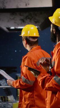 Turuncu ceketli dikey video çalışanı ve sert şapka, petrol çıkarma standartlarına uymayı ve platform güvenliğini sağlayarak, kıyı sondajındaki sistem operasyonlarını analiz ediyor. Kamera B.