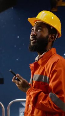 Dikey Video Sanayi Mühendisi, petrol çıkarma faaliyetlerini denizaşırı platformlarda koordine etmek için telsiz kullanıyor ve doğal gaz ve yakıt kontrol operasyonlarını desteklemek için radyo cihazına konuşuyor. Kamera.