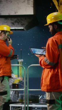 Dikey Video Çevre Memuru, kuzey ışıkları altında kıyı sondajında tablet kullanarak platformda petrol ve yakıt alımını sağlıyor. Petrol ve gaz üretim sanayiine uyum
